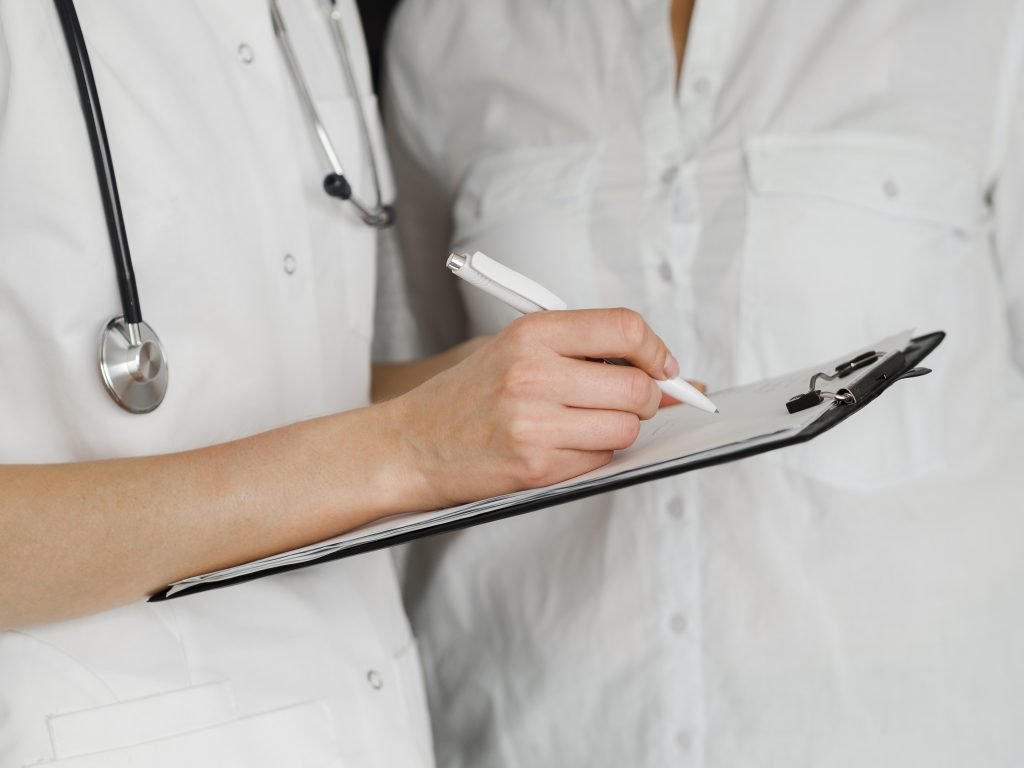 Un médecin écrit sur une feuille à coté d'un professionnel de santé