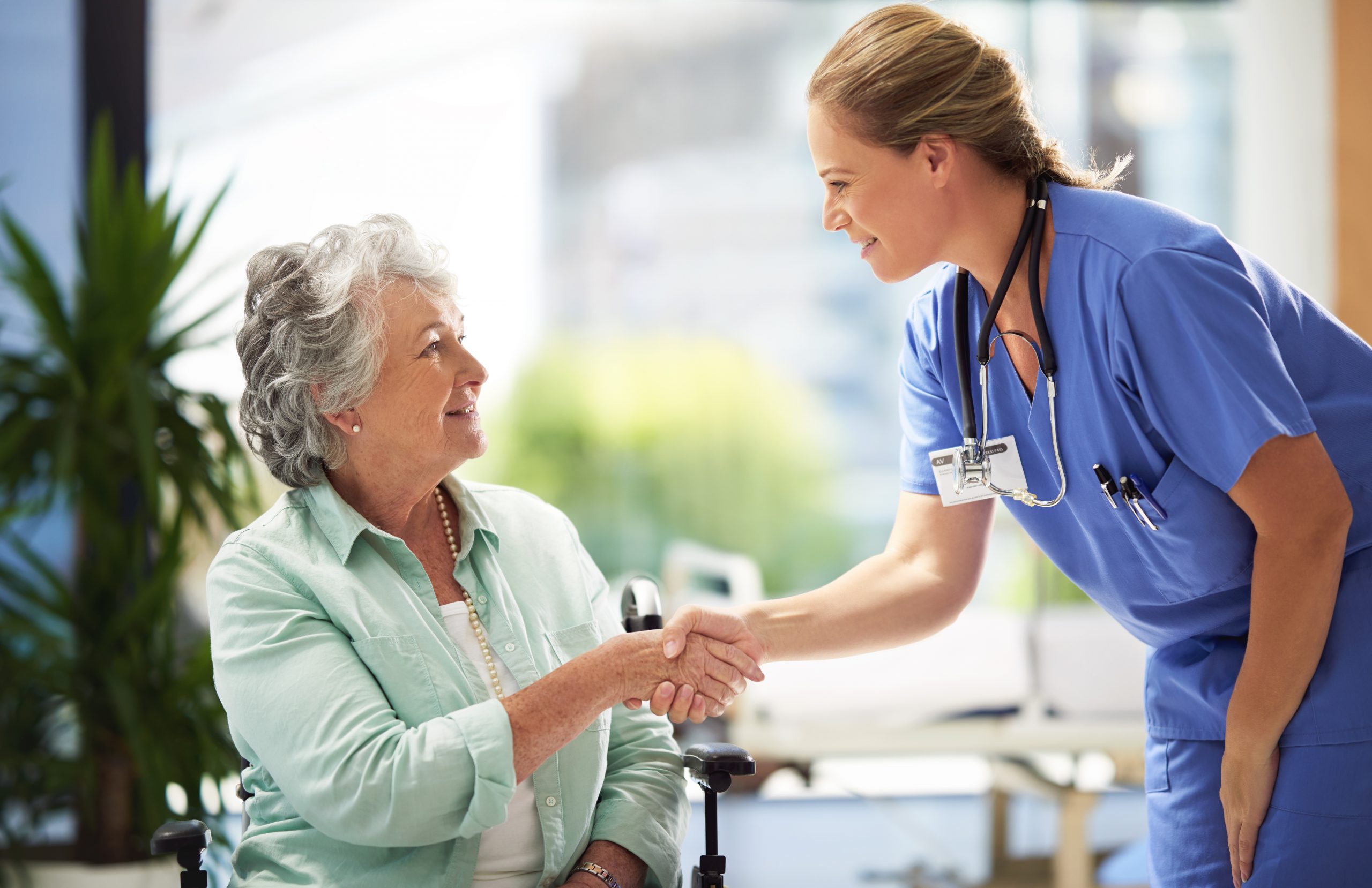 Une infirmière serre la main de sa patiente en chaise roulante